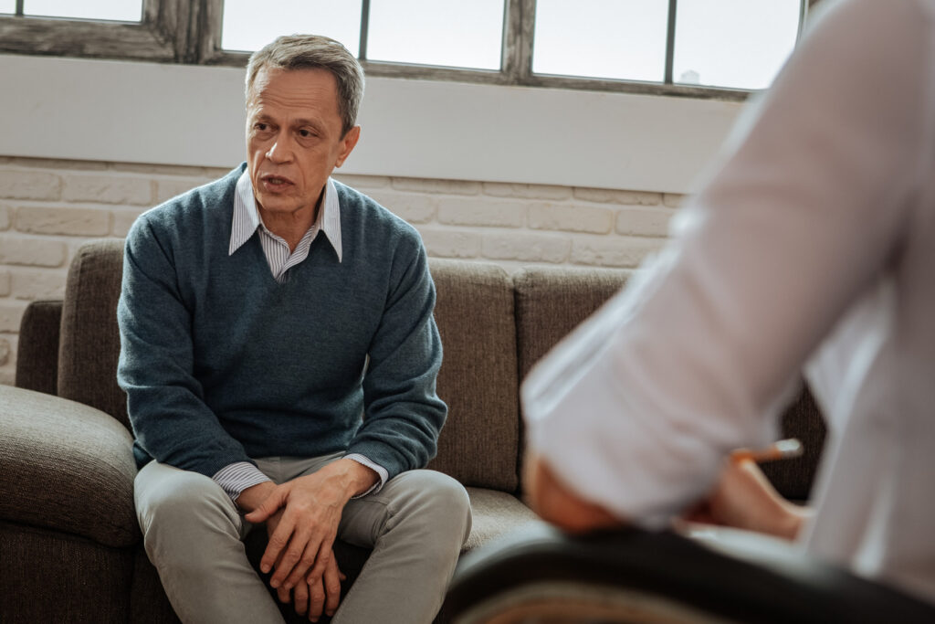 Mature man talking about his life on grey couch.