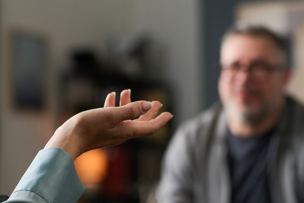 Two people engaging in a counseling session with therapist attentively listening and gesturing with hand, creating an environment of understanding and support